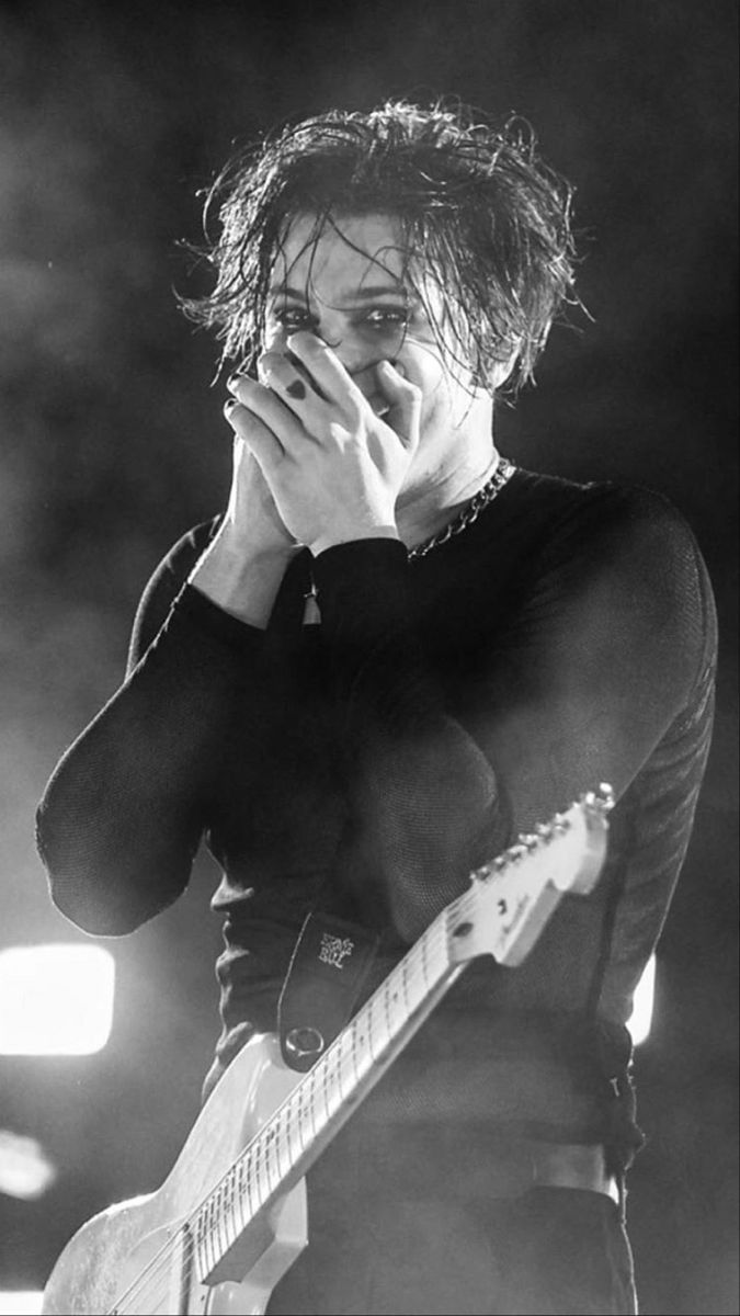 black and white photograph of a man holding his hand to his face as he plays an electric guitar