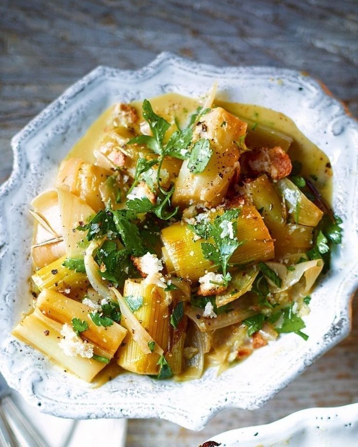 a white bowl filled with pasta and vegetables on top of a wooden table next to utensils