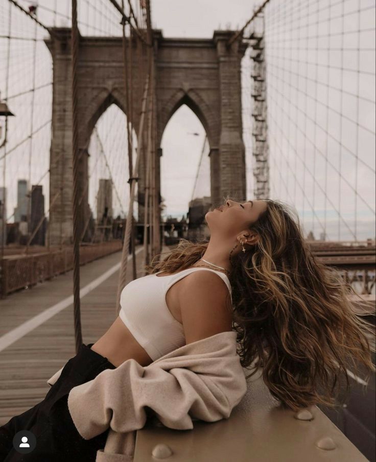 a woman sitting on a bench in front of the brooklyn bridge with her eyes closed