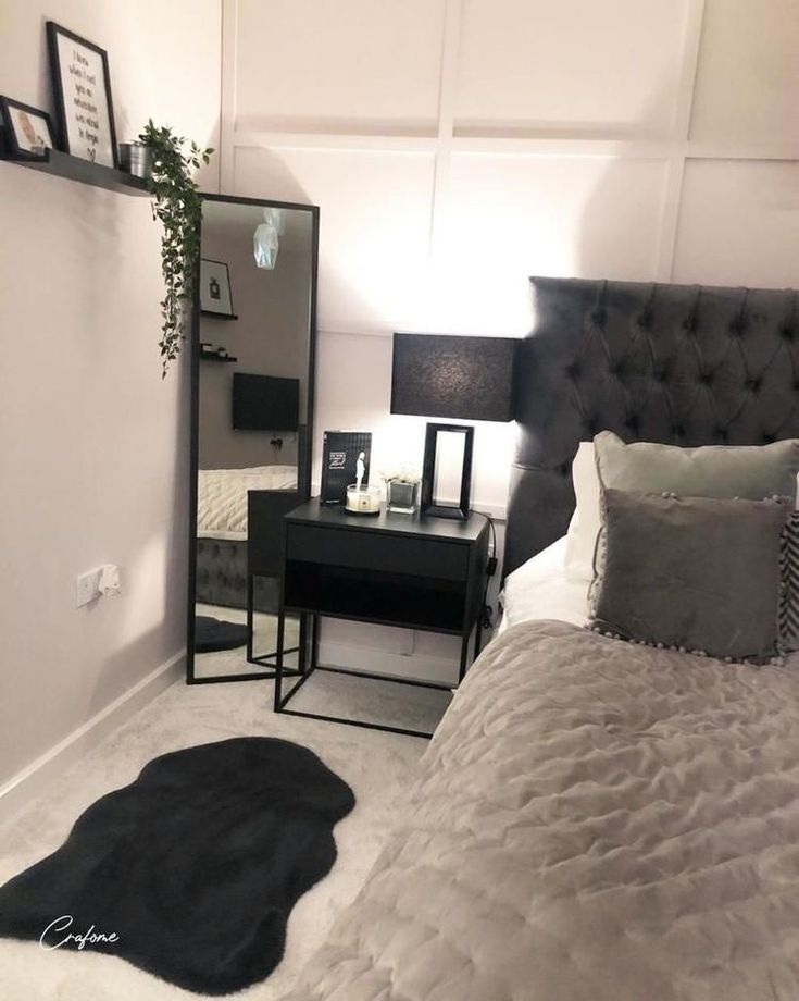 a black and white bedroom with a bed, desk, mirror and plant in the corner