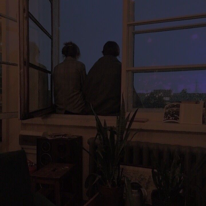 two people sitting on a window sill looking out at the city skyline in the distance