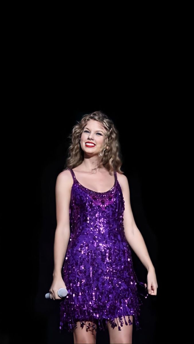 a woman in a purple dress is standing on stage with her hands behind her back