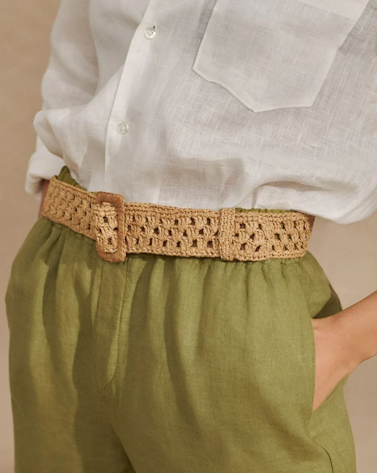 a woman wearing green pants and a white shirt with a crochet belt on her waist