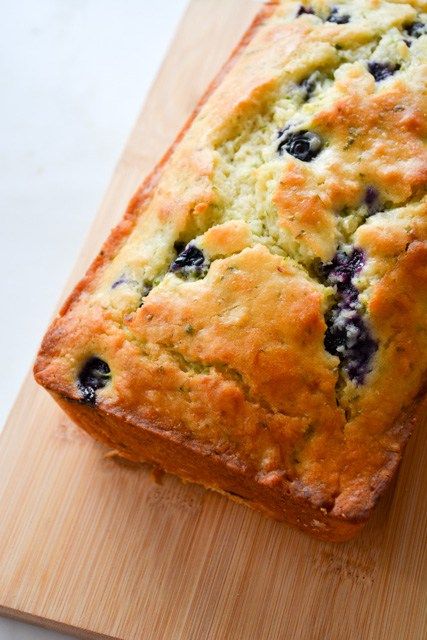 a loaf of blueberry bread sitting on top of a wooden cutting board