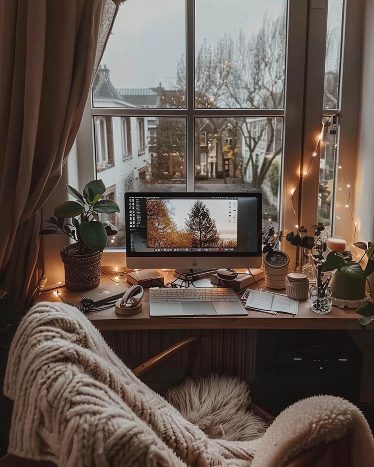 a desk with a computer on it in front of a window filled with christmas lights