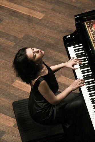 a woman sitting at a piano with her hands on the keys and looking up into the sky