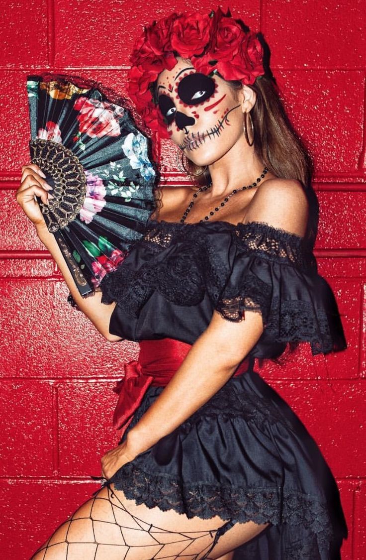 a woman in a black dress holding a fan and wearing fishnet stockings with red roses on her head