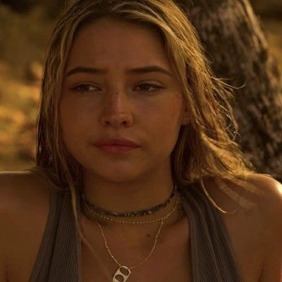 a close up of a person wearing a necklace and looking at the camera with a serious look on her face