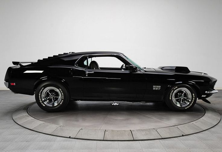 a black muscle car sitting on top of a round floor in a room with white walls