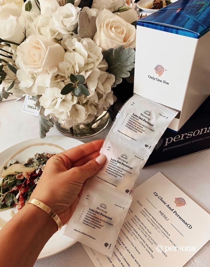 a person is holding some food in front of a table with flowers and menus