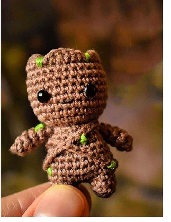 a tiny crocheted teddy bear is being held up by someone's hand