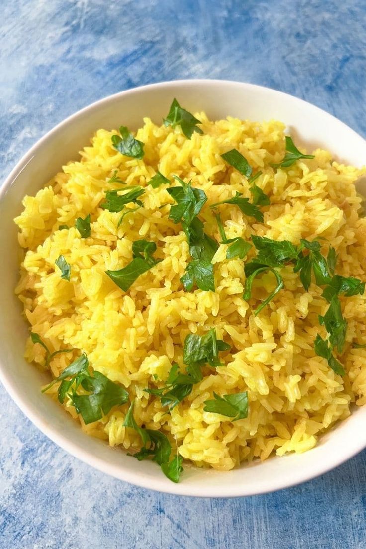 a white bowl filled with yellow rice and green garnish on top of a blue table