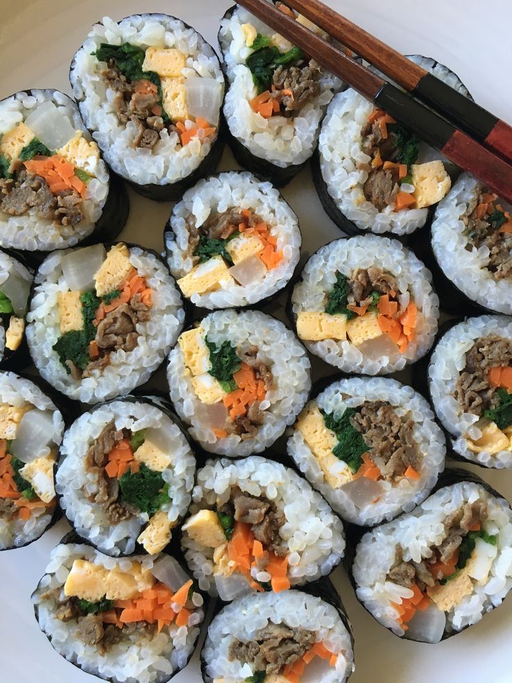 several sushi rolls on a white plate with chopsticks