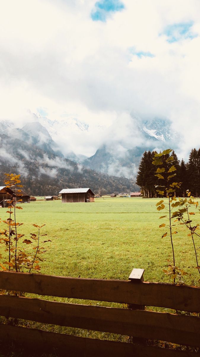 a wooden fence sitting in front of a lush green field with mountains in the background