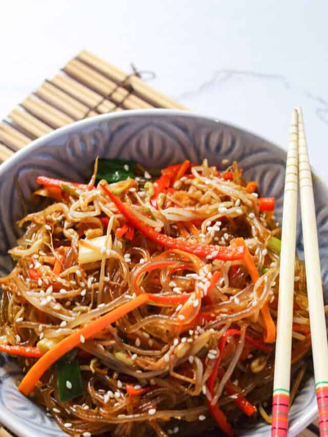 a bowl filled with noodles and vegetables next to chopsticks