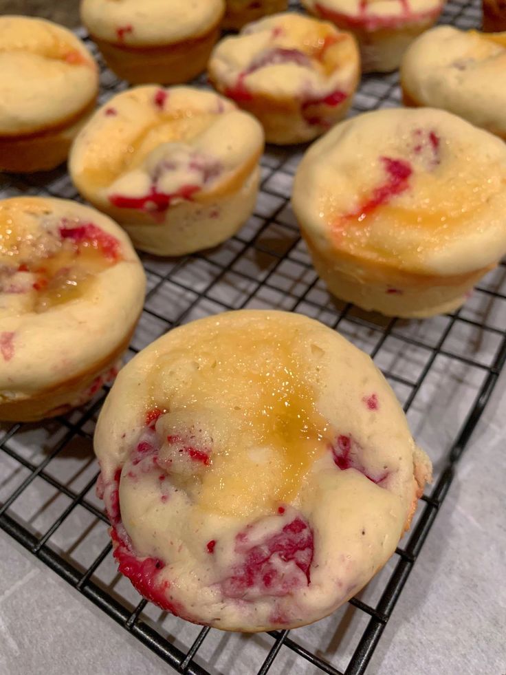 several muffins cooling on a wire rack with icing and strawberry toppings