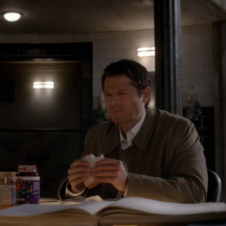 a man sitting at a table in front of an open book and eating something out of his hand