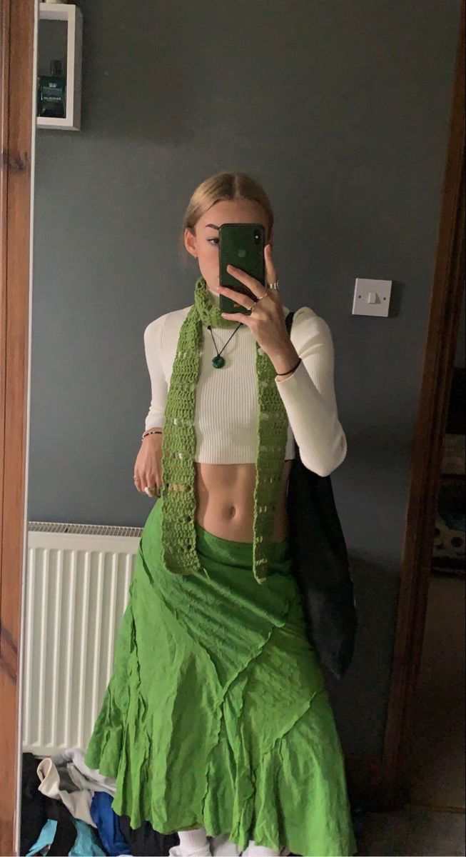 a woman taking a selfie in front of a mirror wearing a green skirt and white top