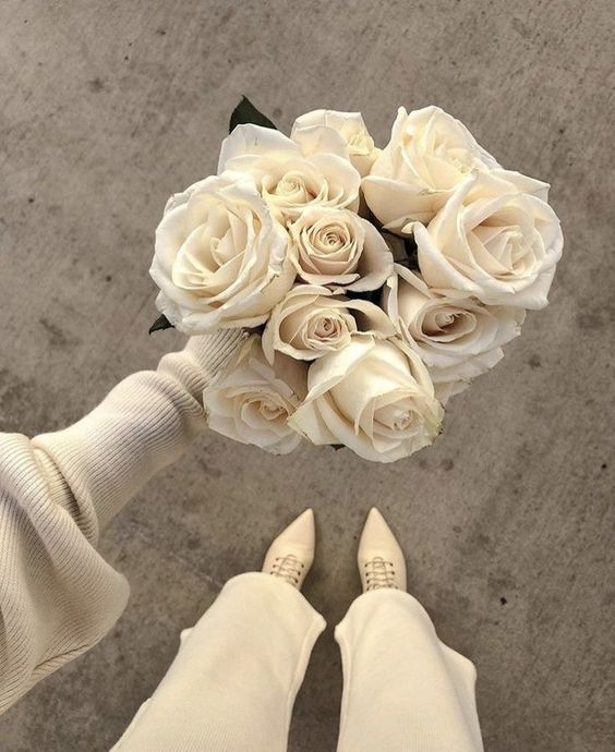 a bouquet of white roses is held by someone's feet on the cement floor