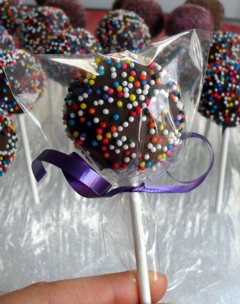 a hand holding a lollipop with chocolate sprinkles and purple ribbon