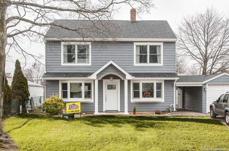 a gray house with a car parked in front of it and a sign on the lawn