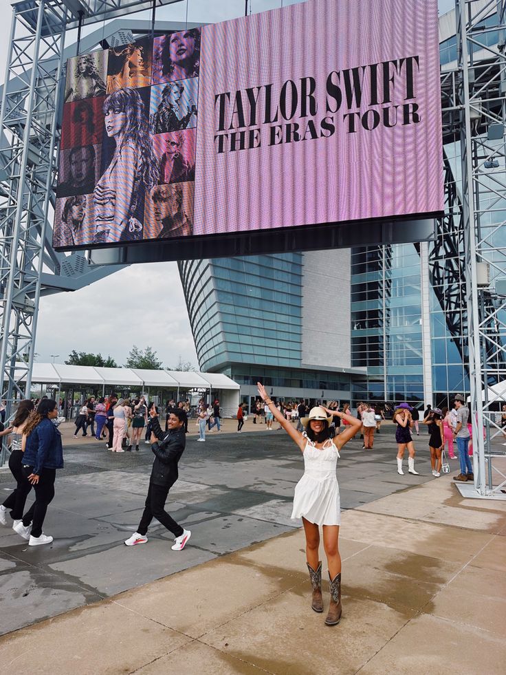 a woman standing in front of a giant billboard with taylor swift the easy tour on it