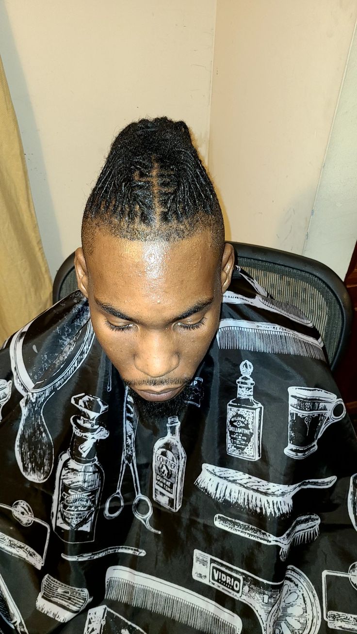 a young man sitting in a barber chair with his hair styled into a bun and cornrow