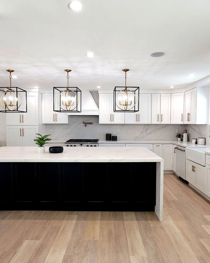 a large kitchen with white cabinets and black island counter tops, wood flooring and pendant lights