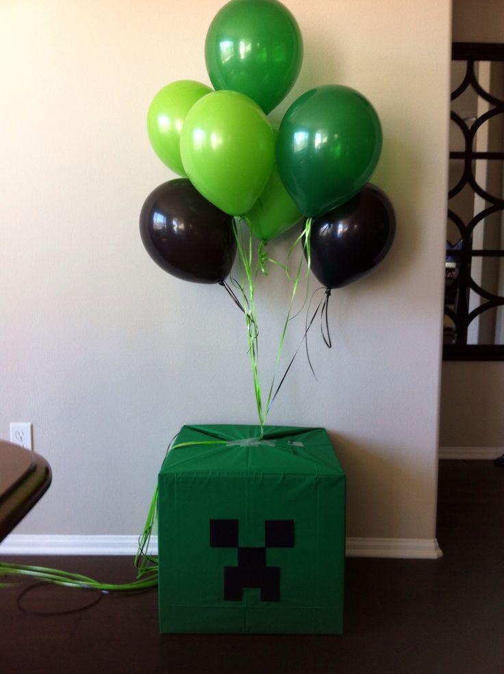 a green box with black and green balloons in it sitting on the floor next to a wall