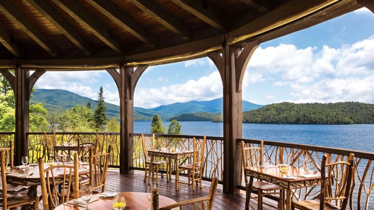 an outdoor dining area with wooden tables and chairs overlooking the water on a sunny day