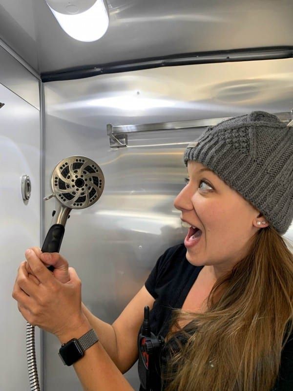 a woman holding a hair dryer in her right hand and looking at it with an excited look on her face