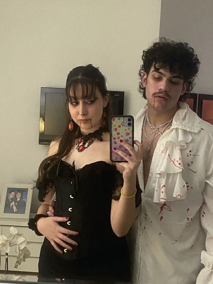 a man and woman standing next to each other in front of a mirror holding cell phones