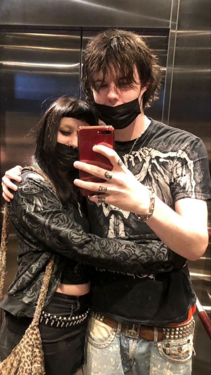 a man and woman wearing face coverings are looking at a cell phone while standing in front of an elevator