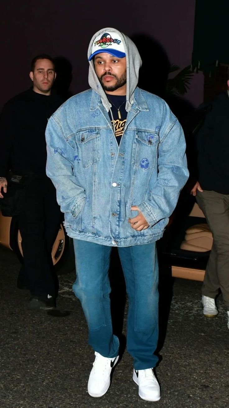 a man wearing a denim jacket and white sneakers is standing in front of some people