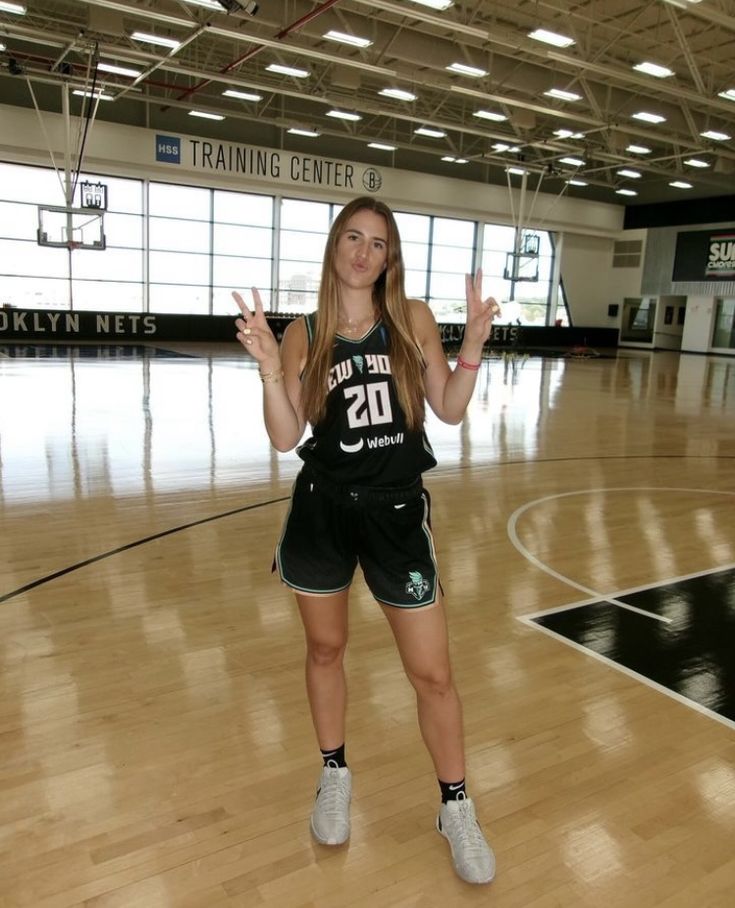 a woman standing on top of a basketball court holding up her hands in the air