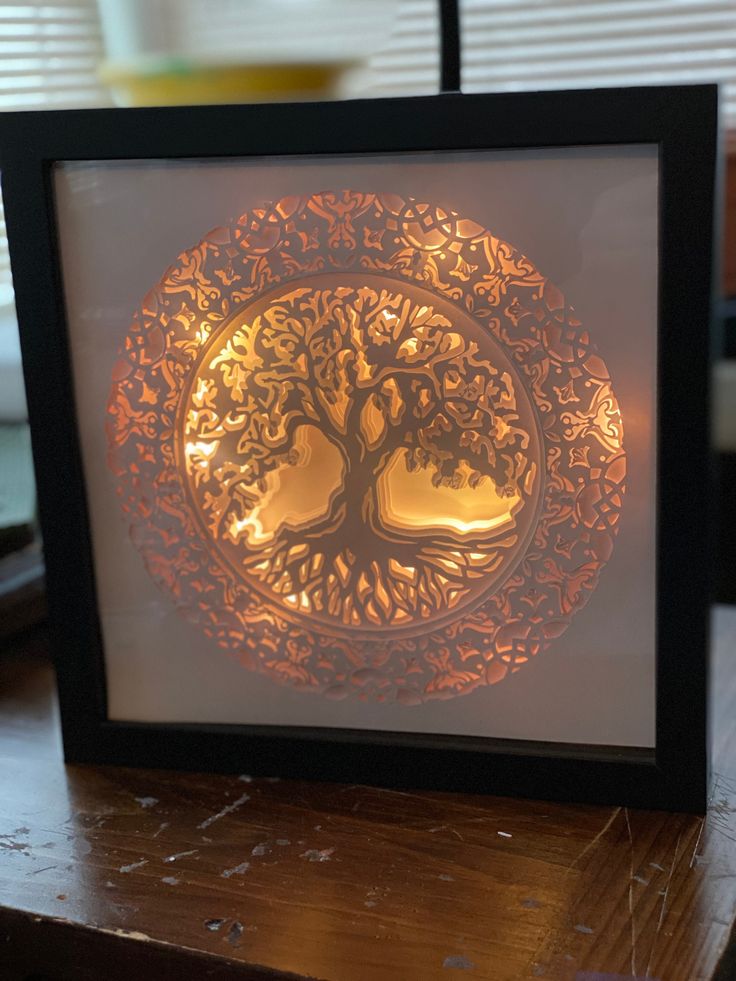 a framed paper cut art with a tree on it's side and lights in the background