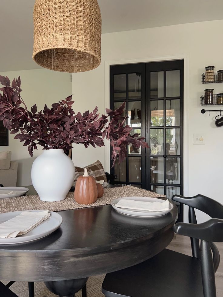 a dining room table with plates and place settings on it, next to a vase filled with flowers