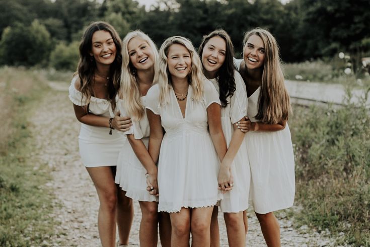 a group of women standing next to each other in front of a dirt road and grass covered field