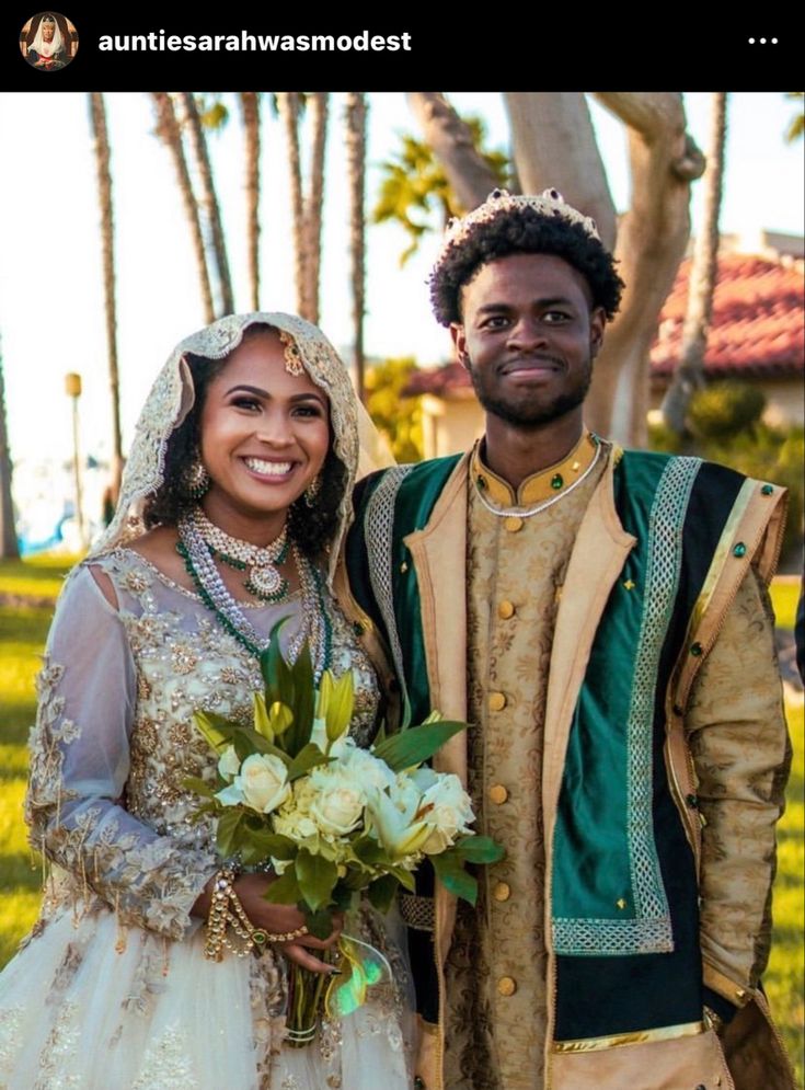 a man and woman dressed in traditional african wedding attire posing for the camera with palm trees behind them