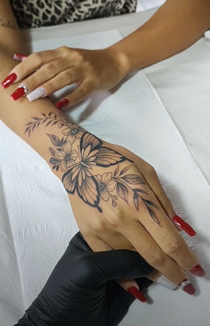 a woman's hand with a flower tattoo on her left arm and red nails