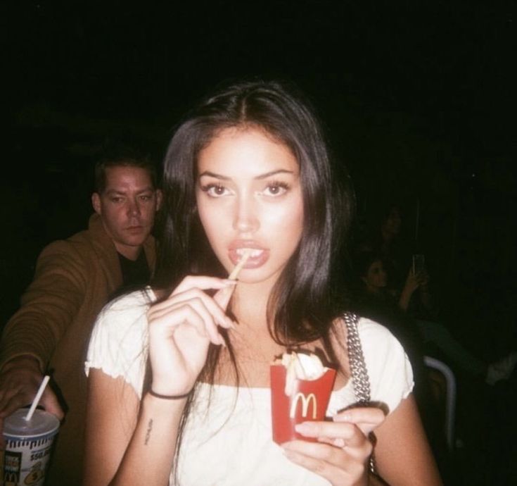 a woman holding a drink in her hand while standing next to a man