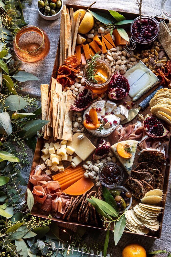 an assortment of cheeses, crackers, and fruit on a wooden tray surrounded by greenery