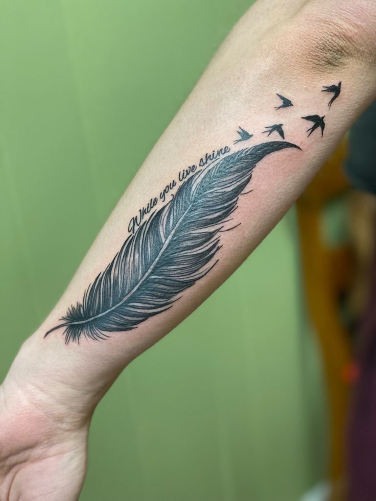 a person's arm with a feather and birds flying in the sky on it