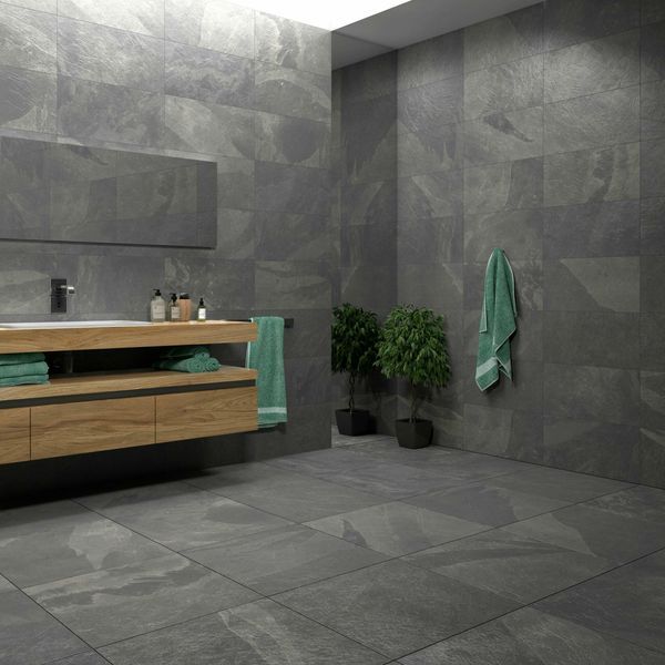 a bathroom with grey tiles and green towels on the counter, along with a potted plant