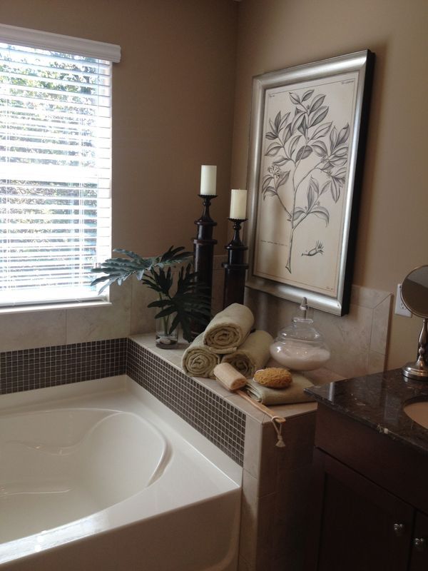 a bath tub sitting next to a window with blinds on the windowsill and candles in front of it