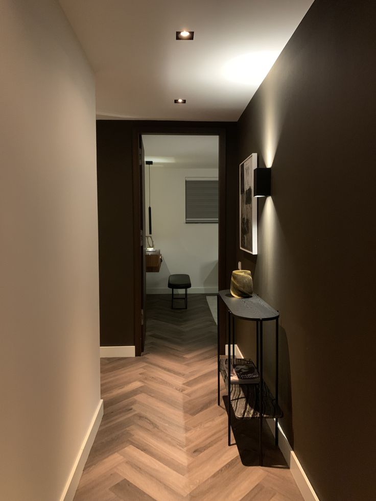 an empty hallway with chevron wood flooring and wall lights on either side of the room