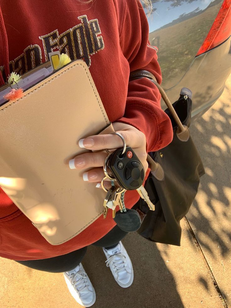 a woman in a red sweatshirt holding a cell phone and a beige purse with keys hanging from it