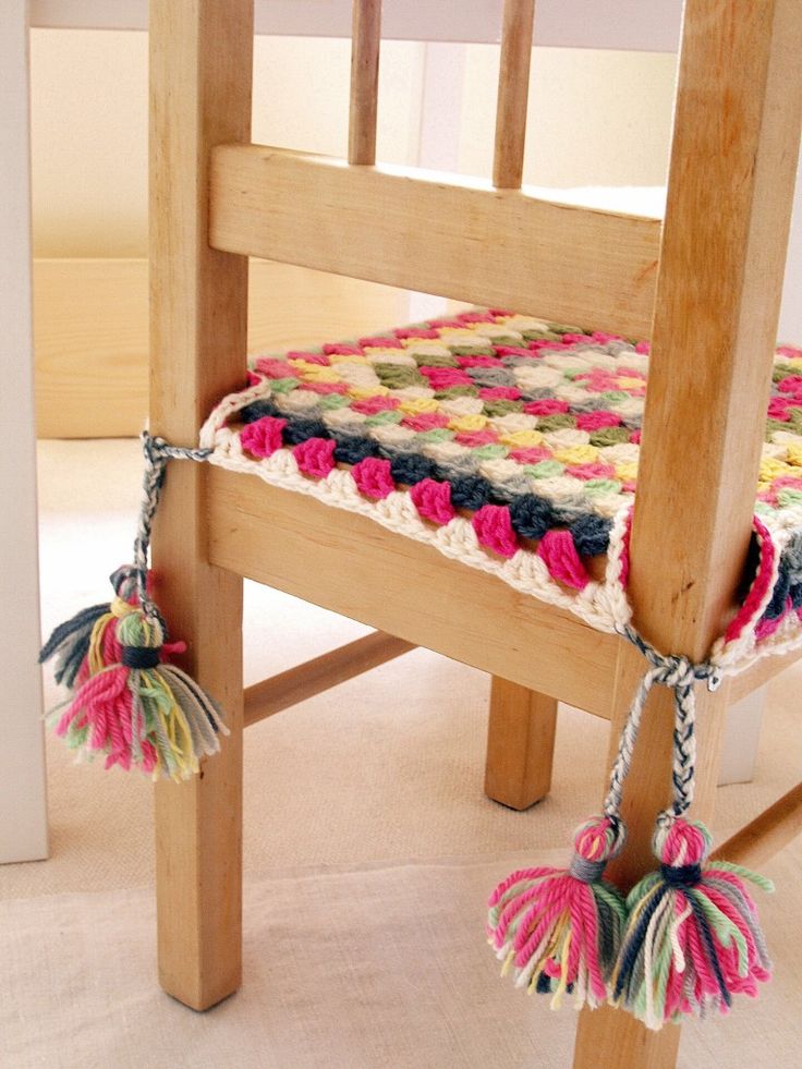 a crocheted seat pad with tassels attached to the back of a wooden chair