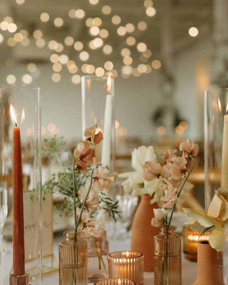 there are many vases with flowers and candles on the table