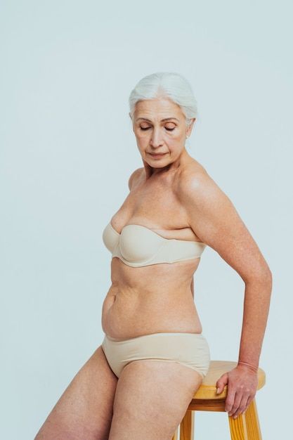 an older woman sitting on top of a wooden stool wearing a tan bra and panties